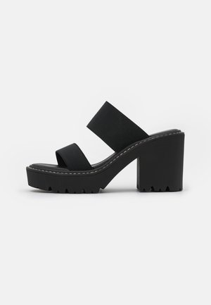 Schwarze Plattform-Sandalen mit zwei breiten Stoffriemen und einer segmentierten Gummisohle. Der Absatz ist blockförmig und strukturiert für besseren Halt.