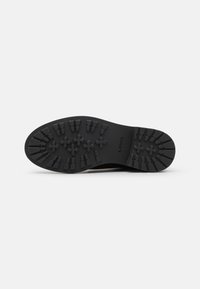 Suela de zapato negra con un patrón texturizado de formas elevadas y surcos para mayor agarre. El material parece goma con un perfil plano y un diseño robusto.