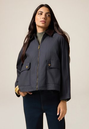 Giacca cropped blu navy con zip frontale, due tasche frontali e colletto in velluto a coste marrone. Texture liscia, design casual.