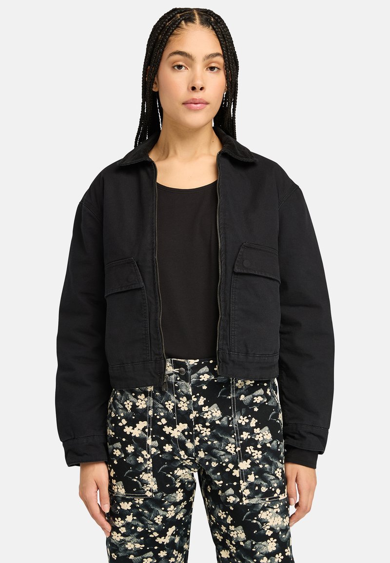 Black cropped jacket with a collared neck, featuring two front pockets and a zip closure, paired with floral-patterned black pants.