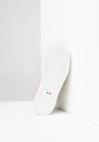 Sneaker med en struktureret hvid gummisål, let beige suedetop og præget logodetaljer. Sålen har et bølget mønster.