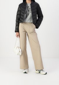 Czarna kurtka puchowa, szara bluza z nadrukiem, beżowe szerokie spodnie, biała torebka i szare buty sportowe z zielonymi akcentami.