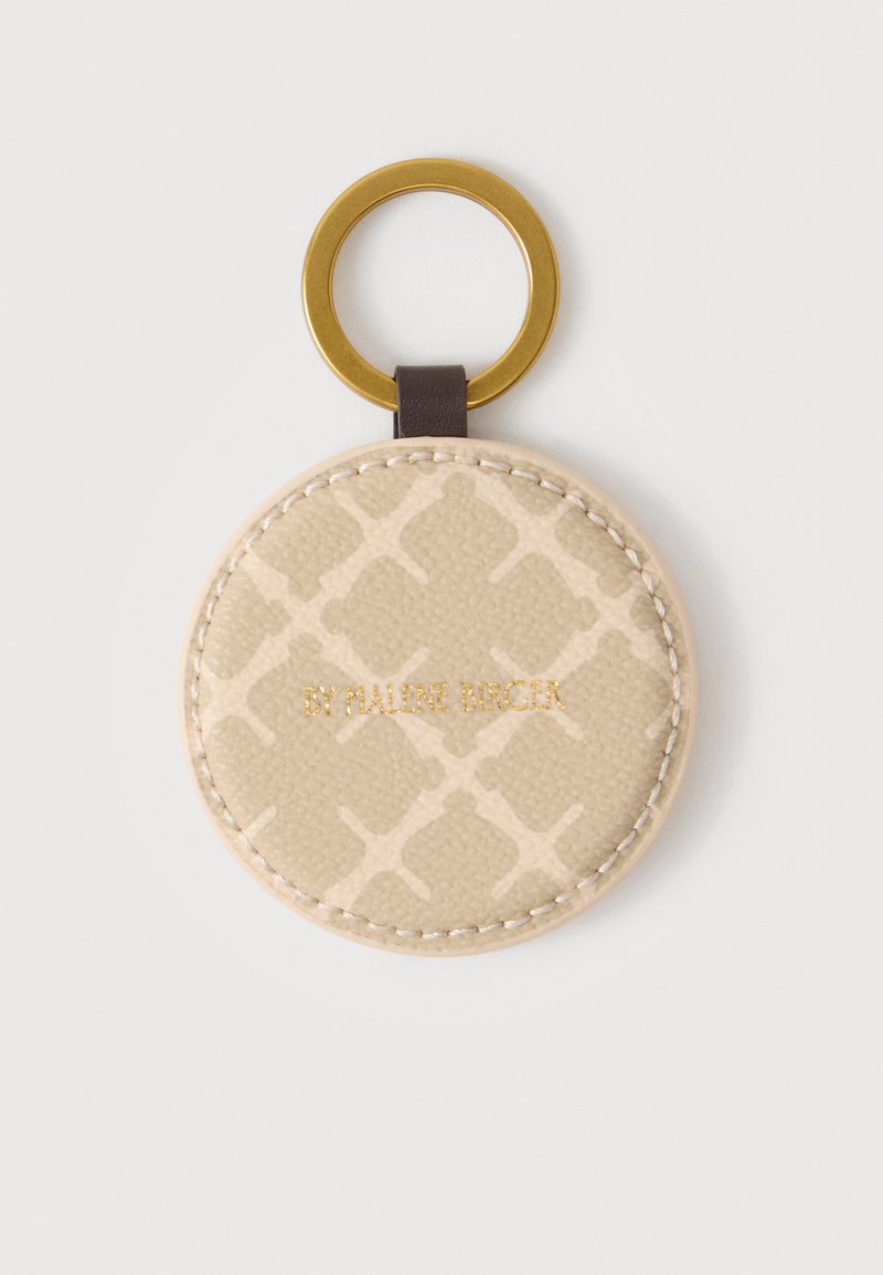 Porte-clés rond en cuir beige avec un motif croisé subtil, texte doré "BY MALENE BIRGER" et anneau en métal doré attaché par une lanière sombre.