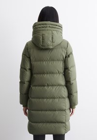 Olijfgroene pufferjas met een capuchon, met horizontale stiksels en een middellange ontwerp. De stof lijkt soepel en gewatteerd.
