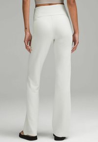 Valkoiset ridatut flare-housut, joissa on leveä vyötärönauha ja teksturoitu kangas. Helma ulottuu mustien tasapohjaisten kenkien ylle. Näkymä takaa.