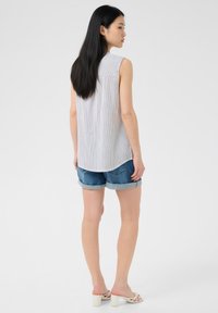 Top senza maniche e leggero con righe verticali, abbinato a shorts di jeans arrotolati. L'outfit presenta una vestibilità comoda e tonalità neutre.