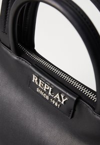 Zwarte leren handtas met bovenhandvatten, voorzien van een zilveren ritssluiting en een gegraveerd label waarop "REPLAY SINCE 1981" staat. Gladde textuur.