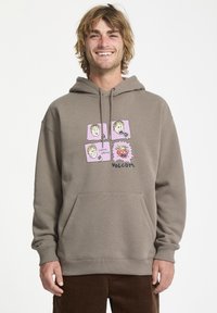 Sudadera marrón con un bolsillo frontal, que presenta un gráfico de cuatro caras de dibujos animados sobre un fondo rosa claro. El nombre de la marca "Volcom" está incluido.