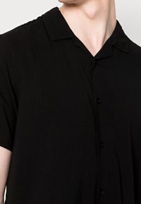 Czarna koszula na krótki rękaw z miękką teksturą, prostym kołnierzykiem i eleganckimi czarnymi guzikami; zaprojektowana na luźny krój.