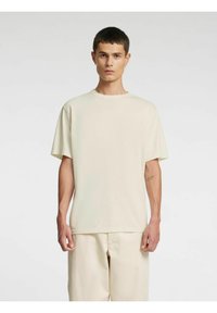 Helebeežid lühikese varrukaga T-särk, ümmarguse kaelusega, lõdva istuvusega, pehmest puuvillakangast, nähtavate õmblustega, kantud sobivate helebeežide pükstega.