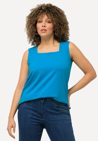 Top blu senza maniche con scollatura quadrata, realizzato in tessuto liscio. Abbinato a jeans in denim scuro. Design semplice e pulito senza decorazioni.