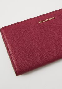 Burgundy leather wallet with textured finish, featuring a gold "MICHAEL KORS" logo, rectangular shape, and stitched edges.