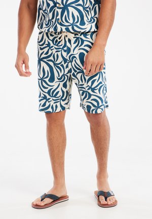 Shorts en mélange de coton avec un fond blanc et un motif de feuilles abstraites bleu foncé. Dotés d'une taille ajustable avec un cordon de serrage.