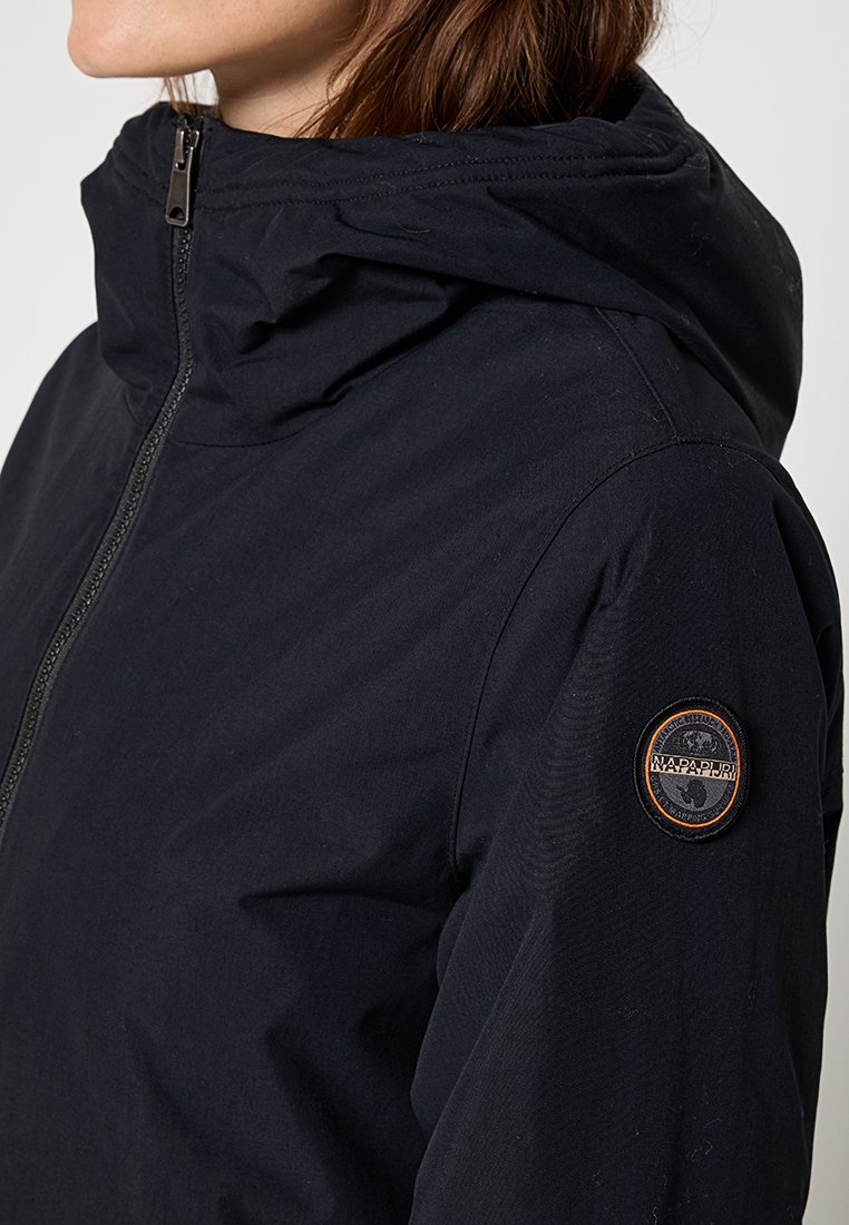 Veste à capuche noire avec fermeture éclair, texture lisse et une patch en tissu orange sur l'épaule gauche.