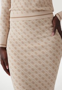 Knit sweater ja hameyhdistelmä vaaleassa sävyssä, jossa on ruskea geometrinen kuvio. Setissä on ribattu hihansuu ja vyötärö, mikä antaa teksturoidun ulkonäön.