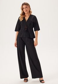 Svart tvådelad outfit som består av en kortärmad wrap-topp med knytning och vida byxor gjorda av lätt material.