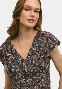 Granatowa bluzka z kwiatowym wzorem w odcieniach pomarańczowym i kremowym. Posiada dekolt w kształcie litery V oraz krótkie bufiaste rękawy. Wykonana z miękkiego, teksturowanego materiału z falbaną.