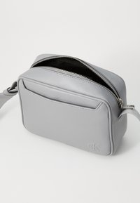 Grå læder crossbody taske med en struktureret overflade, en forlomme og en dobbelte lynlås lukning. Har en rem for nem transport.