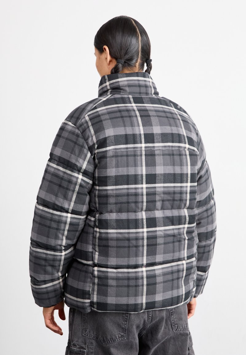 Szara puchowa kurtka w kratę z wysokim kołnierzem, charakteryzująca się pikowanym wzorem oraz czarno-szaro-białym wzorem w kratę. Zapewnia ciepło i komfort.