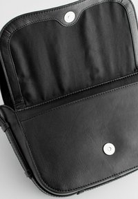 Černá kožená taška s hladkým povrchem, vybavená uzávěrem na patentku a jednoduchým, plochým interiérem. Minimalistický design, bez viditelných vzorů.