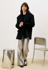 Blazer noir oversize, pantalon large métallisé, et chaussures noires à motifs. Design minimaliste avec textures lisses et finitions brillantes.