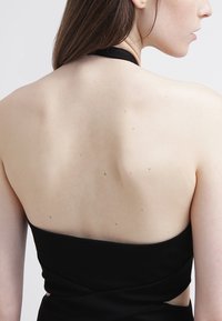 Zadní pohled na přiléhavé černé šaty s hlubokým výstřihem na zádech. Hladká textura a minimalistický design zdůrazňují kontury těla.