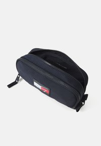 Navyblaue Nylon-Tasche mit einem Zwei-Wege-Reißverschluss, auf der Vorderseite mit einem rechteckigen Logopatch in Rot, Weiß und Blau.