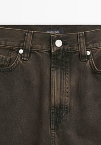 Mörkbruna denimjeans med en standard femficksdesign, subtila blekningar, metallhardware och en märkesetikett vid midjan.