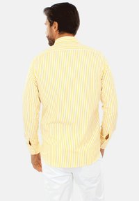 Camicia a maniche lunghe a righe gialle e bianche realizzata in tessuto con una texture liscia; presenta un colletto classico e dettagli con bottoni sui polsini.