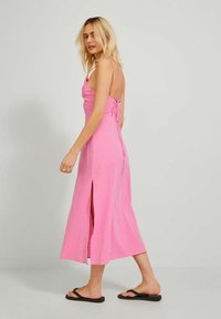 Vestido midi rosa con un corpiño ajustado, tirantes finos y un escote en la espalda. Presenta una tela texturizada y aberturas laterales para mayor movilidad.