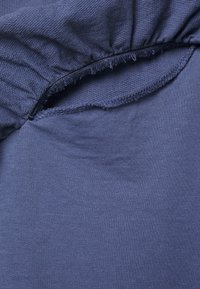 Roupa azul marinho com decote franzido, apresentando uma textura de algodão suave e detalhe de borda crua na abertura.
