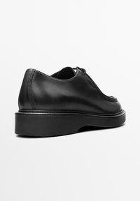 Black leather shoe with a rounded toe, low heel, and minimal design. Features smooth texture and subtle stitching along the seams.