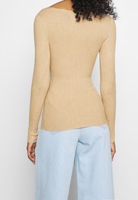 Kobieta ubrana w dopasowaną, beżową bluzkę z ribbed oraz jasnoniebieskie, wysokie dżinsy o szerokich nogawkach, pokazana od tyłu.