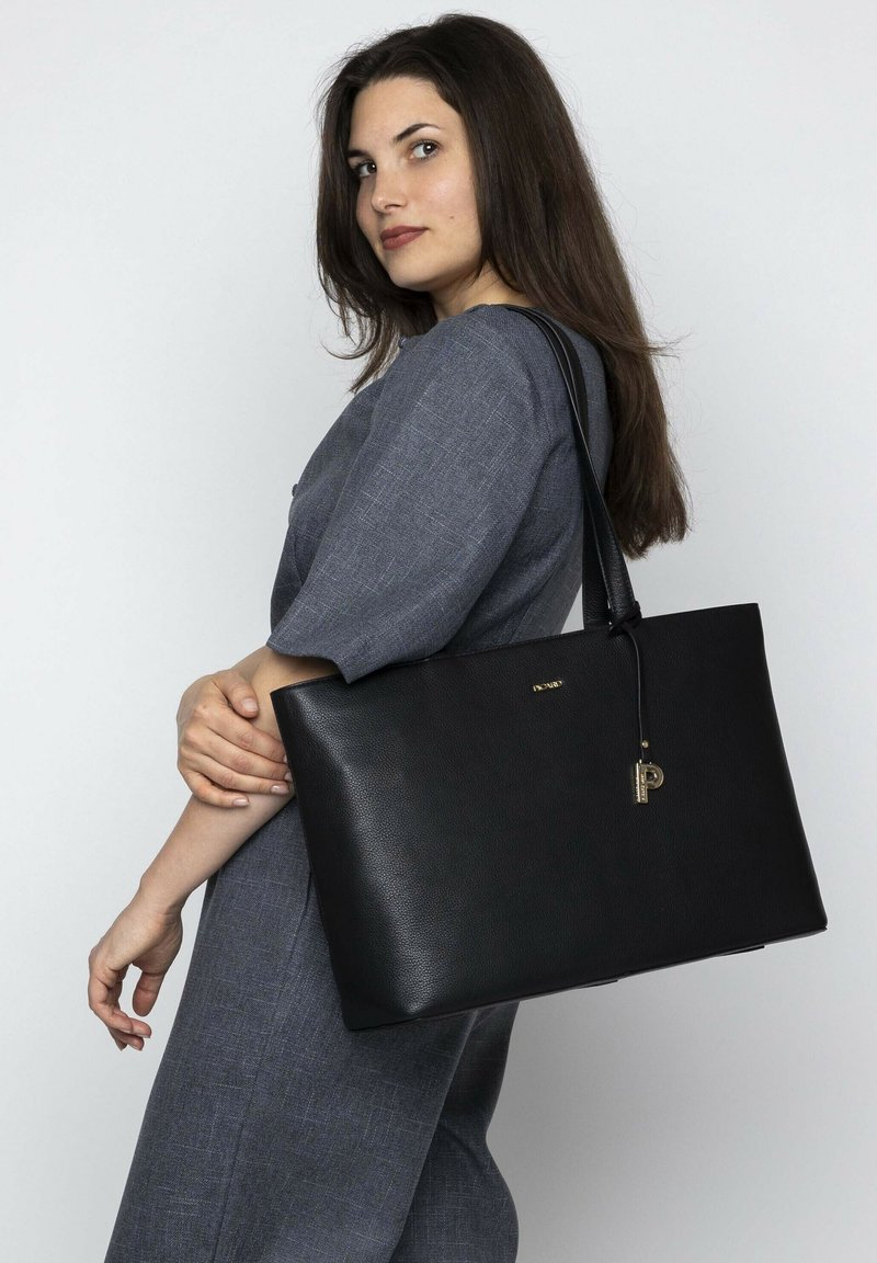 Zwarte leren tote bag met textuur, platte vorm en lange handgreep. Heeft een gouden accent en een sleutelhanger-detail.