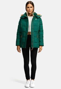Green puffer jacket with a fur-lined hood, zippered pockets, and ribbed cuffs. Paired with black skinny pants and white sneakers.