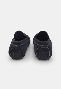 Mörkblå mockaloafers med synlig vit sömnad, rundad baksida, mjuk textur och gummisula för bra grepp. Enkelt design.