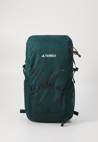 Tamnozeleni ruksak s teksturiranim materijalom, s prilagodljivim sustavom užadi, mrežastim bočnim džepovima i bijelim "TERREX" logotipom na prednjoj strani.