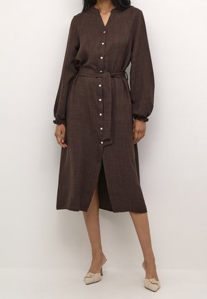 Femme portant une robe marron midi à manches longues boutonnée avec une ceinture à la taille et des mules beiges à bout pointu et talons.