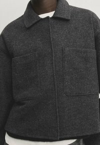 Grijze wolmix jas met een kraag, knoopsluiting aan de voorkant en twee grote opgestikte zakken op de borst.