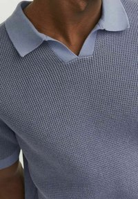 Pletená polo košile v světle modré barvě s výstřihem do V a kontrastním límcem. Krátké rukávy mají texturovaný vzor a žebrovaný konec.