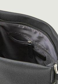 Interno di una borsa nera in tessuto con una cerniera metallica liscia e una piccola tasca interna con una cerniera simile e un'etichetta cucita.