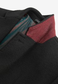 Mustmust coat maroon viltkaelusega, millel on sile tekstuur. Sisevooder on tealmugavusega, mis paistab välja kaeluse juures.