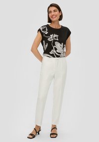 Zwarte top met bloemenpatroon en korte mouwen, gecombineerd met witte kledingstoffen pantalon en zwarte haksandalen. Eenvoudig en modern ontwerp.