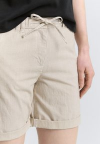 Beige stribede shorts lavet af vævet stof, med snor i taljen og optrukne manchetter. Afklippet kant med diskret syning.
