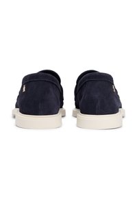 Chaussures en daim bleu marine avec un talon bas, semelle en caoutchouc beige et détails de couture simples. Petit logo métallique sur le côté.