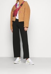 En tanfärgad, fluffig fleecejacka, vit t-shirt med grafik, svarta vida byxor och vita sneakers med neonkonturer. Axelväska i rosa.