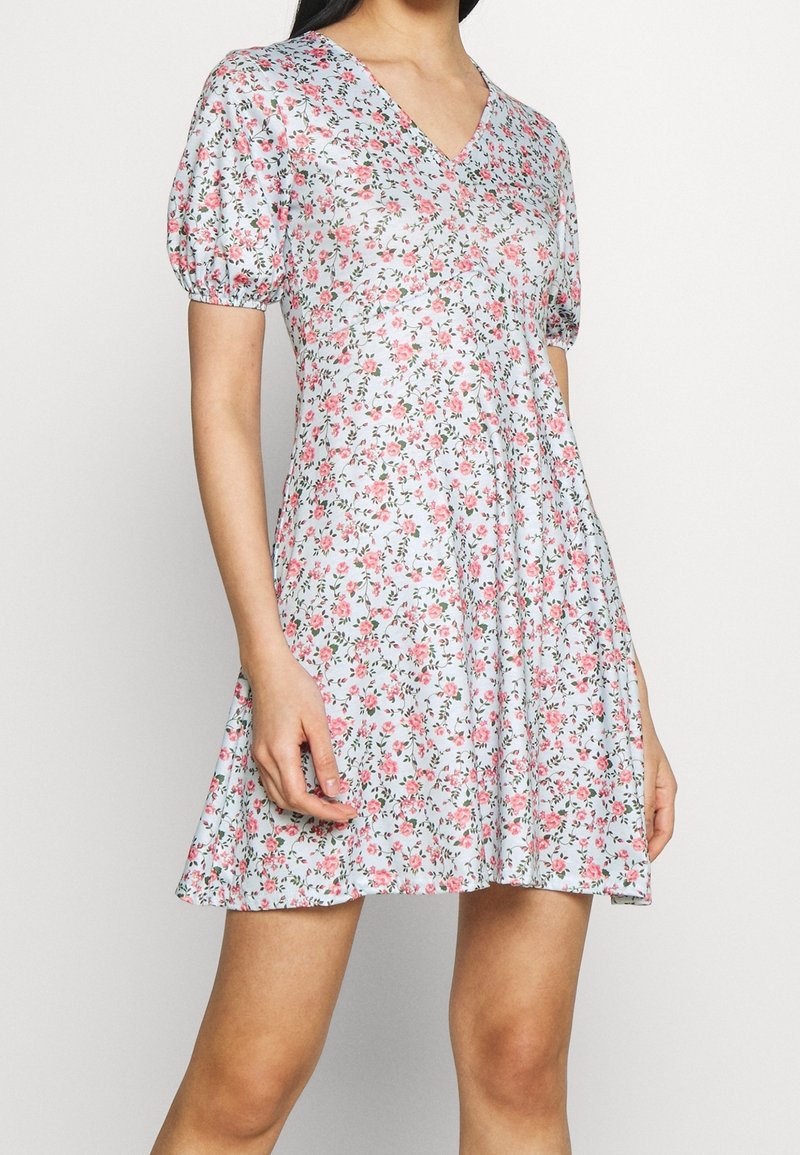 Blommig klänning med ljusblå bakgrund, featuring en V-ringning, puffärmar och en utsvängd kjol. Mönster av rosa rosor och gröna blad.