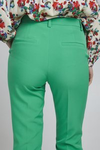 Groene op maat gemaakte broeken met een gladde textuur, slim fit en achterzakken, gecombineerd met een bloempatron blouse met rode en blauwe accenten.
