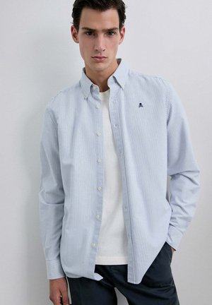 Camisa de botones a rayas en azul claro y blanco, con un pequeño logo en el pecho y un corte relajado. Fabricada con tejido ligero.