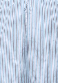 Tissu bleu clair avec des rayures verticales espacées régulièrement en blanc et brun foncé, montrant un gros plan d'une couture ou d'un pli.